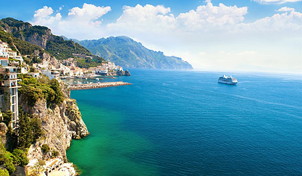 A quaint town on a cliff with a cruise ship far out in the distance in blue waters