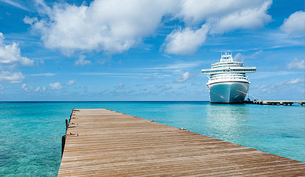 A wooden dock that leads to blue ocean water with a generic cruise ship at a dock in the distance