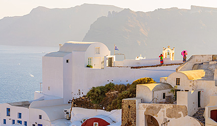 An overlook in Greece with white walled buildings, mountains and the ocean