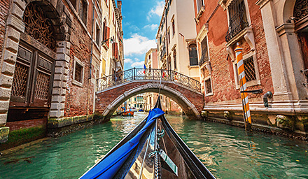 The front half of a traditional gondola in the waterways of Venice surrounded by red brick buildings