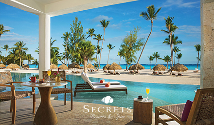 A swim up hotel room patio with breakfast food items, lounge chairs, palm trees and ocean