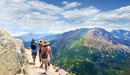A group of people hiking with fluffy clouds and rocky mountains in the background
