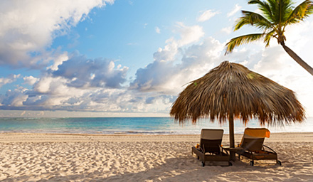 Tropical umbrella with two lounge chairs, a palm tree, clear blue water and sand